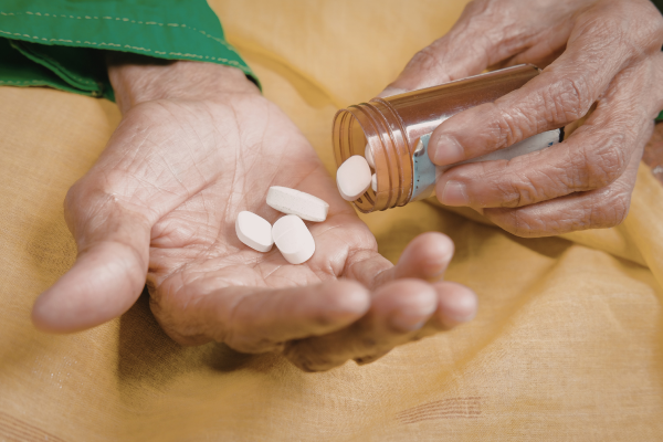Manos de una persona mayor sosteniendo pastillas de un frasco, reflejando la correcta administración de medicamentos en el cuidado domiciliario.