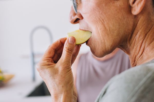 Adulto mayor comiendo un trozo de manzana fresca en la cocina para ilustrar el cuidado nutricional y la salud articular
