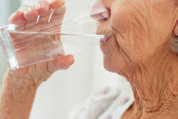 Adulto mayor bebiendo un vaso de agua fresca para ilustrar la importancia de la hidratación en verano y la prevención de la deshidratación