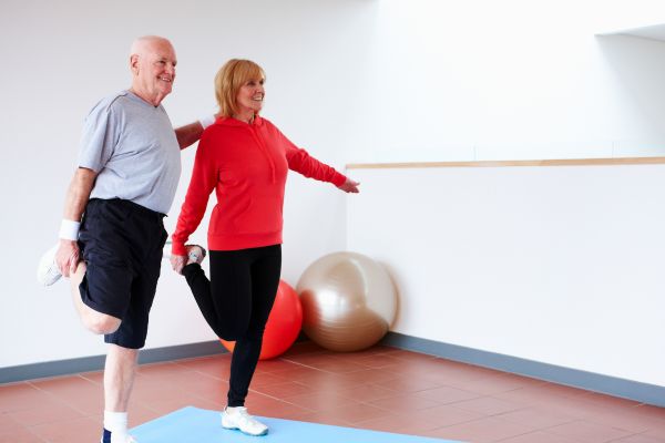 Adultos mayores practicando ejercicios de estabilidad y estiramiento en una esterilla para la prevención de caídas y mejora del equilibrio